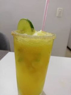 a tall glass with a cucumber on the rim and a straw in it