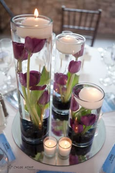 two vases filled with flowers and candles on a white table cloth covered round table