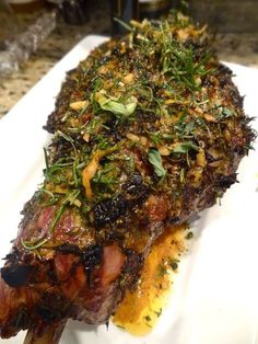 a piece of meat on a white plate with herbs and seasoning sprinkles