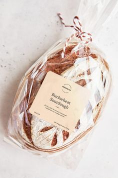 a loaf of bread wrapped in plastic on top of a white countertop next to a tag