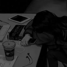 a woman sitting at a desk with her head down on the table next to a cup and cell phone