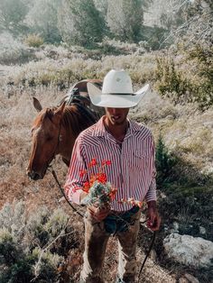 a man wearing a cowboy hat and holding flowers in his hand next to a horse