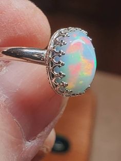 a close up of a person's hand holding an opal ring