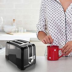 a woman holding a red cup next to a black and white toaster on a counter