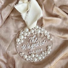 a glass ornament with pearls and a white ribbon on a satin fabric background