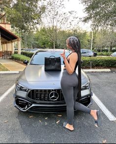 a woman leaning on the hood of a car with her hand in her pocket and purse