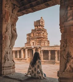 a woman sitting on the ground in front of an ancient building