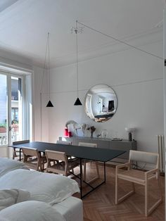 a dining room table and chairs in front of a large window with an oval mirror on the wall