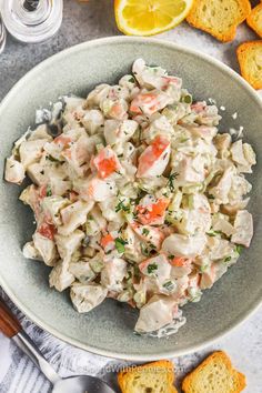 a bowl filled with chicken salad next to crackers and lemon wedges on the side