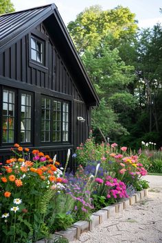 a black house with many different flowers in the front yard and side walk leading up to it