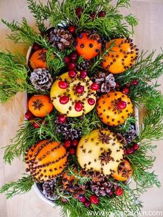 a bowl filled with oranges and pine cones on top of a wooden table covered in greenery