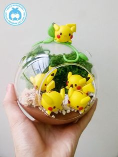 a hand holding a glass ornament with small pikachu figurines in it