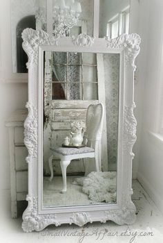 an ornate white mirror with a chair and table in front of it on the floor