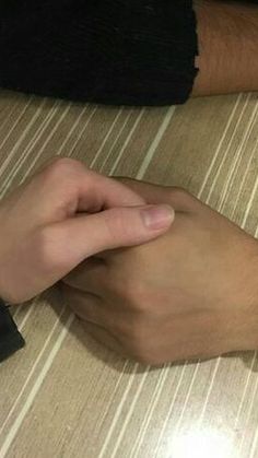 two people holding hands on top of a wooden table next to a cell phone and an apple watch