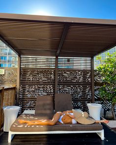 a woman laying on top of a brown couch under a wooden awning next to a tree