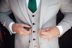 a man in a gray suit and green tie is tying his button on the lapel