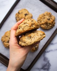 a person holding three cookies in their hand on a baking tray with marble counter top