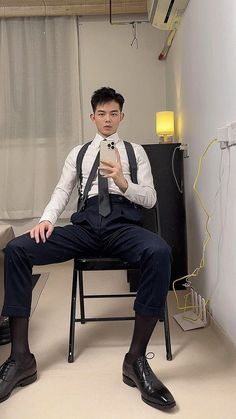 a man sitting in a chair with his legs crossed and holding a cell phone up to his face