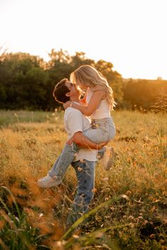 a man and woman kissing in the middle of a field with tall grass at sunset