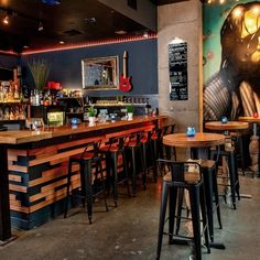 an empty bar with stools and tables in front of the bar area that has a painting on the wall