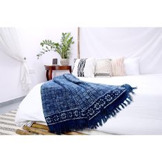 a white bed topped with a blue blanket next to a wooden night stand and potted plant