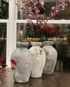 three vases sitting on top of a wooden table next to a window with flowers in them