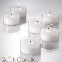 four white candles in glass containers with one lit candle on top and the other surrounded by smaller ones