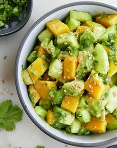 a bowl filled with cucumber and other vegetables on top of a white table