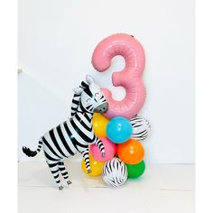 a zebra standing next to a bunch of balloons in front of a number 3 sign