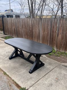 a black table sitting on top of a sidewalk next to a wooden fence and trees