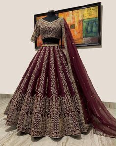 a maroon and gold lehenga is displayed on a mannequin in front of a painting