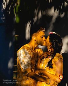 a man and woman kissing in front of a tree