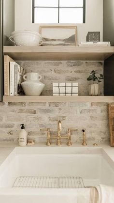 a white sink sitting under a window next to a shelf filled with books and other items