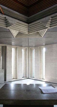 an empty room with two windows and a table in the middle is surrounded by concrete columns