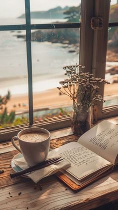 an open book and cup of coffee sit on a window sill overlooking the beach