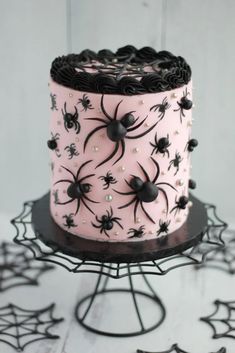 a pink cake decorated with black spider webs and pearls on a metal stand in front of white background