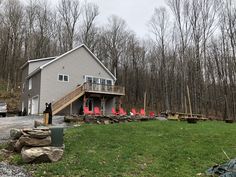 a house in the middle of a wooded area with red chairs on the front lawn