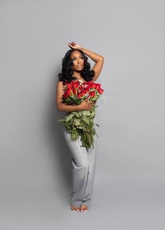 a woman is holding flowers in her hands and posing for the camera on a gray background