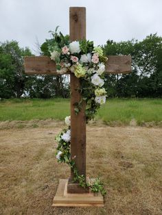 a cross decorated with flowers and greenery in the middle of an open field on a cloudy day