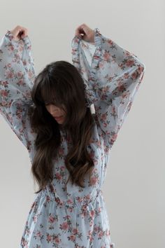 a woman with long hair wearing a blue floral dress and holding her hands behind her head