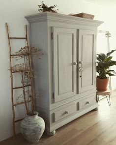 a white armoire sitting on top of a wooden floor next to a potted plant