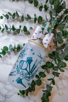 a jar with some hair clips on top of it next to green plants and leaves