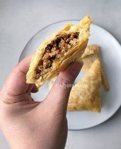 a hand holding a piece of food on top of a white plate next to a fork