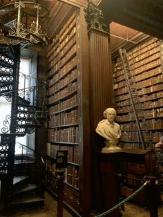 an old library filled with lots of books next to a busturine and spiral staircase