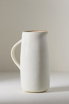 a white coffee mug with a wooden handle on a plain tableclothed surface in front of a gray background