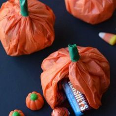 candy candies wrapped in orange and green paper with pumpkins around them on a black surface