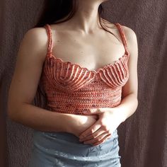 a woman standing in front of a brown wall wearing a tank top and blue skirt