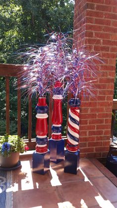 three red, white and blue vases with flowers in them sitting on a porch