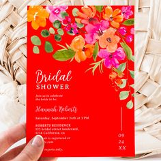 a person holding up a red and orange floral bridal shower card in front of a wicker basket