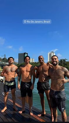 four men standing on a dock in front of the water with their bare chests and no shirts